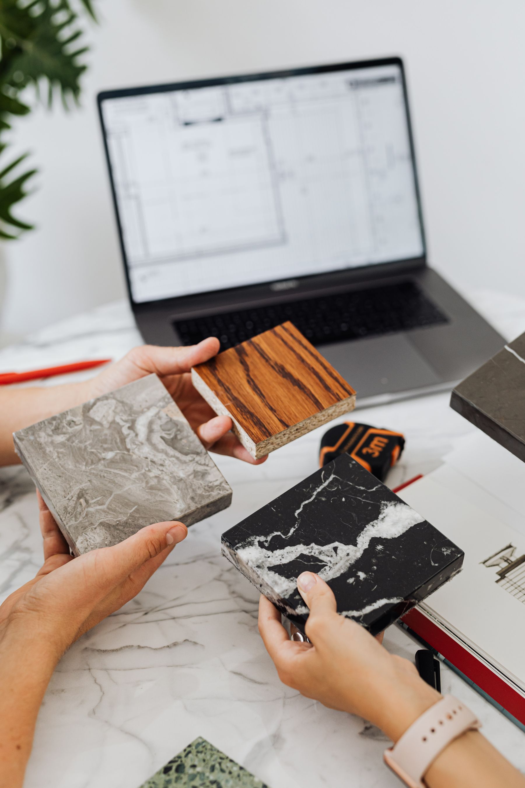 Hands comparing stone and wood-look finish samples beside a laptop